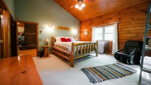 Een slaapkamer met een houten plafond, een bed met wit beddengoed, een zwarte massagestoel, een stenen muur en een raam met witte gordijnen.