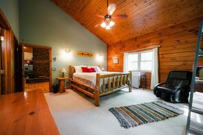 A bedroom with a wooden ceiling, a bed with white bedding, a black massage chair, a stone wall, and a window with white curtains. - Big Rock | Theater Room, Hot Tub, Hocking Hills (Rockbridge)