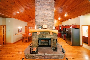 A stone fireplace with a log arch, wooden ceiling, and a kitchen area with modern appliances. - Big Rock | Theater Room, Hot Tub, Hocking Hills (Rockbridge)