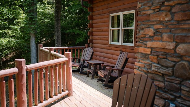 Een houten terras met Adirondack-stoelen en een tafel, een stenen muur en een raam.