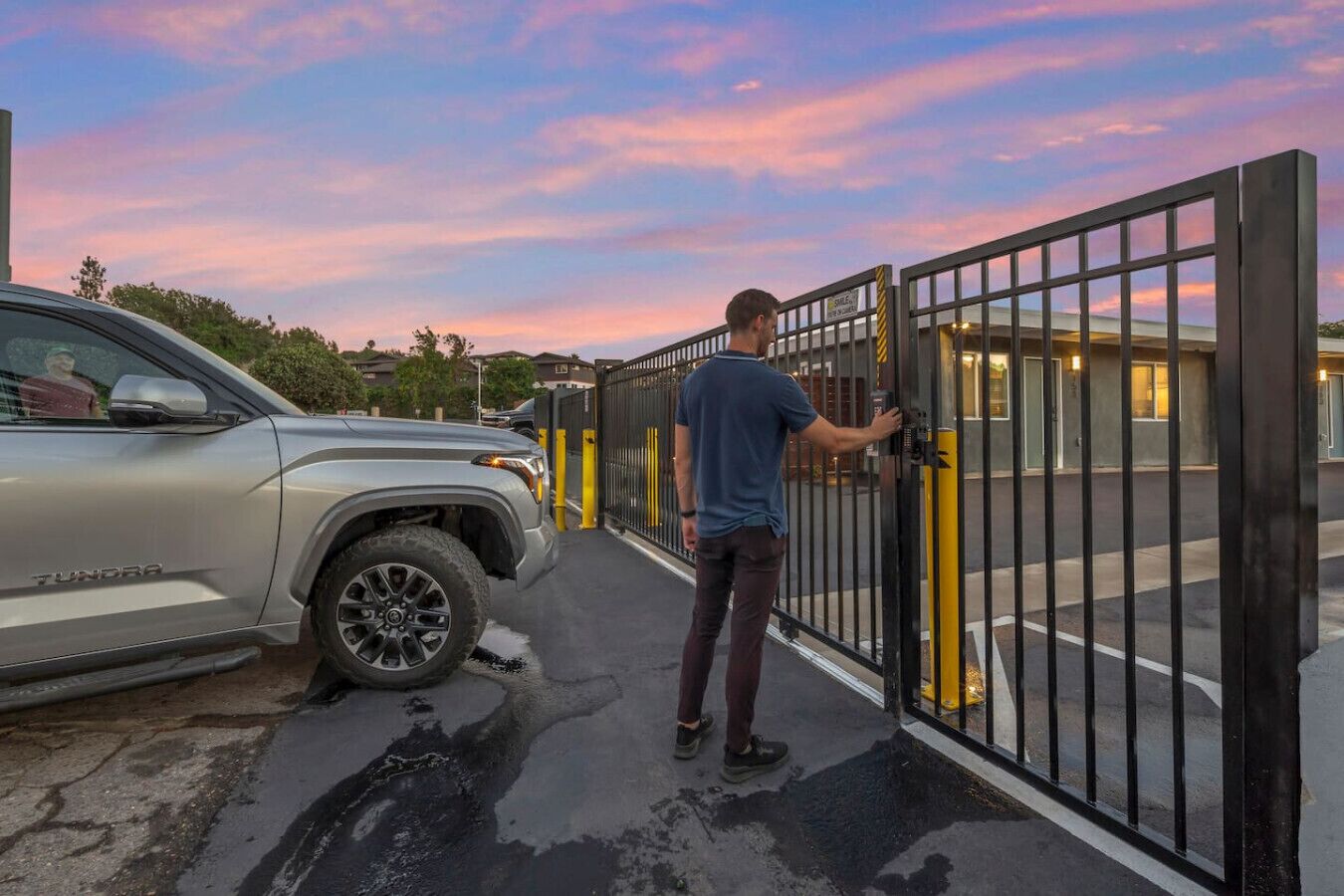 En person åbner en låge til en bygning, med en bil parkeret i nærheden.