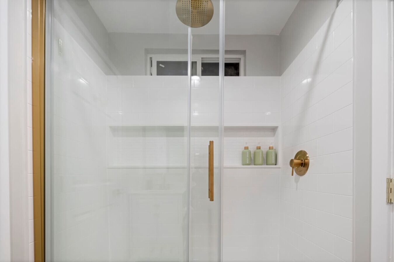 Une salle de bain moderne avec des carreaux blancs, une douche en verre et une poignée de porte dorée.