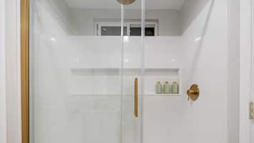 Une salle de bain moderne avec des carreaux blancs, une douche en verre et une poignée de porte dorée.