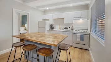 Una cocina moderna con una isla de madera, taburetes de bar, armarios blancos y electrodomésticos de acero inoxidable.