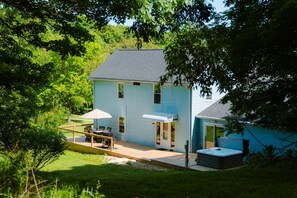 A light blue house with a patio, a hot tub, and a covered outdoor seating area. - Whispering Acres | Hocking Hills, Hot Tub, Firepit (Logan)