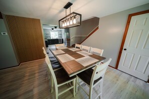 A dining area with a long table, chairs, and a hanging light fixture. - Whispering Acres | Hocking Hills, Hot Tub, Firepit (Logan)
