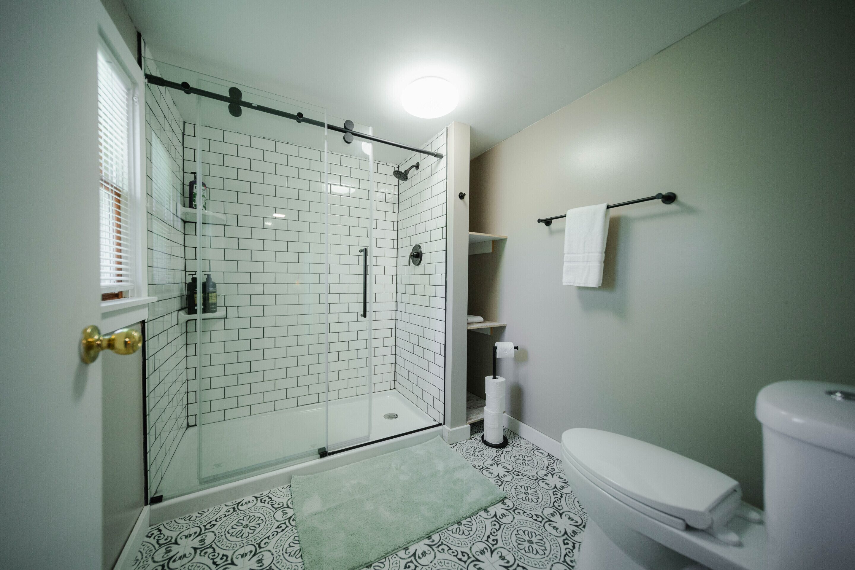Un baño con ducha acristalada, inodoro y baldosas de suelo estampadas.