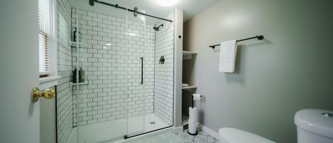 Un baño con ducha acristalada, inodoro y baldosas de suelo estampadas.
