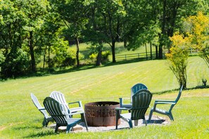 A fire pit with chairs around it in a grassy area with trees in the background. - Whispering Acres | Hocking Hills, Hot Tub, Firepit (Logan)