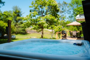 A hot tub with a wooden deck and outdoor furniture in the background. - Whispering Acres | Hocking Hills, Hot Tub, Firepit (Logan)