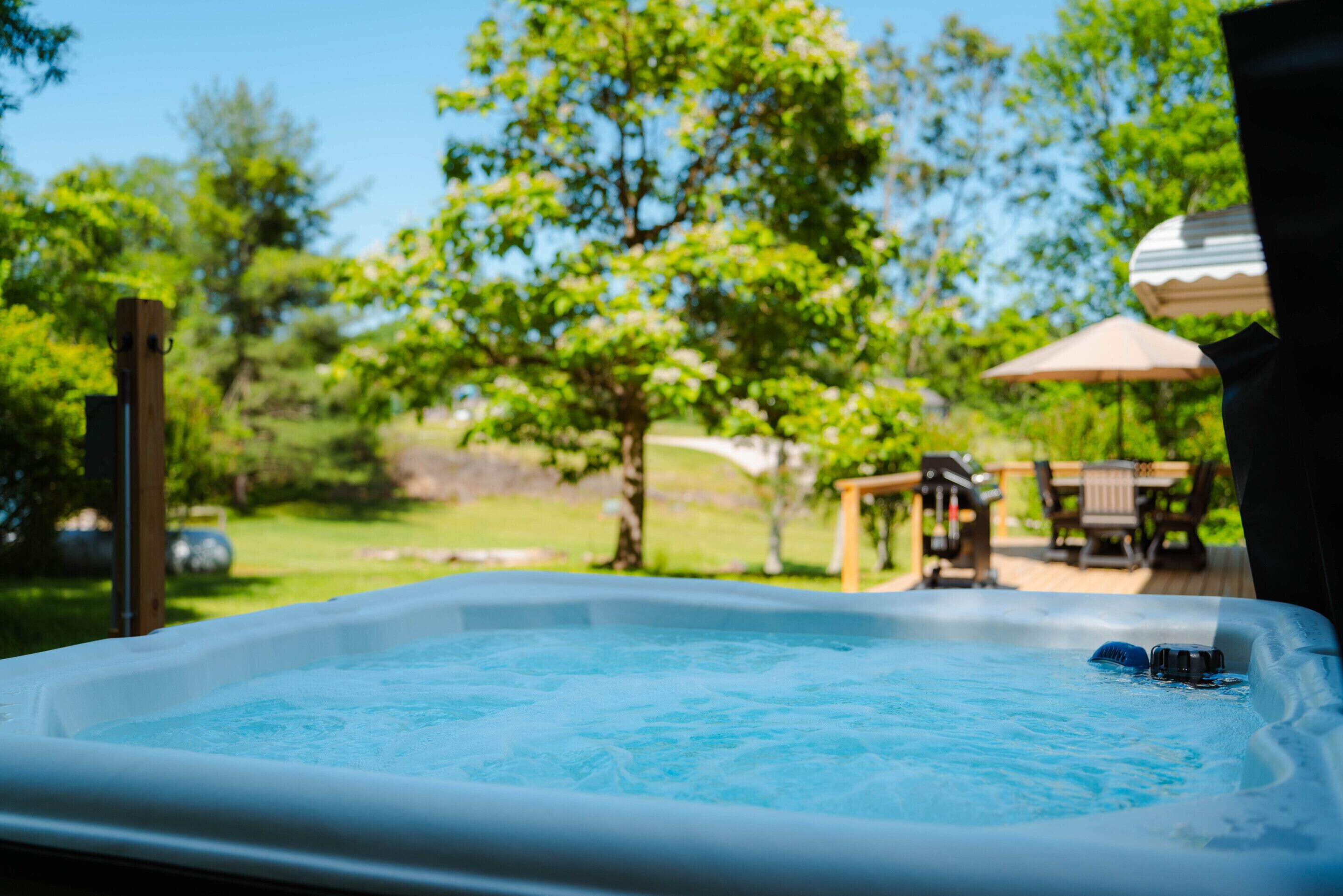 A hot tub with a wooden deck and outdoor furniture in the background.