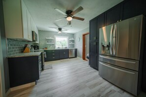 A kitchen with dark cabinets, a stainless steel refrigerator, a ceiling fan, and a window. - Whispering Acres | Hocking Hills, Hot Tub, Firepit (Logan)