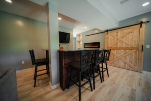 A modern kitchen with a wooden bar, a flat-screen TV, and a sliding barn-style door. - Whispering Acres | Hocking Hills, Hot Tub, Firepit (Logan)