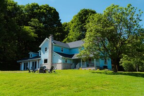 A two-story house with a porch, surrounded by a grassy lawn and trees. - Whispering Acres | Hocking Hills, Hot Tub, Firepit (Logan)