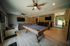 Une table de billard dans une pièce dotée d’un ventilateur de plafond, d’un téléviseur à écran plat et d’un coin bar.