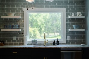 A kitchen with a window, a sink, and various items on shelves. - Whispering Acres | Hocking Hills, Hot Tub, Firepit (Logan)