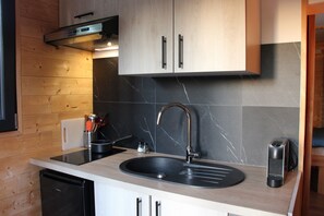 A kitchen with a black sink, stainless steel faucet, wooden cabinets, and a built-in stove. - Tiny Home 'D'Artagnan De La Pausa Verda' with Shared Terrace, Private Garden and Wi-Fi (Montréal)