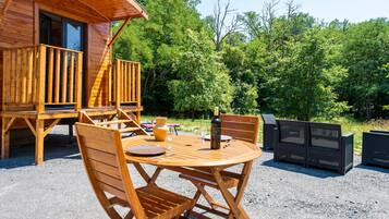 A wooden cabin with a deck, a round wooden table with chairs, and a black wicker sofa.