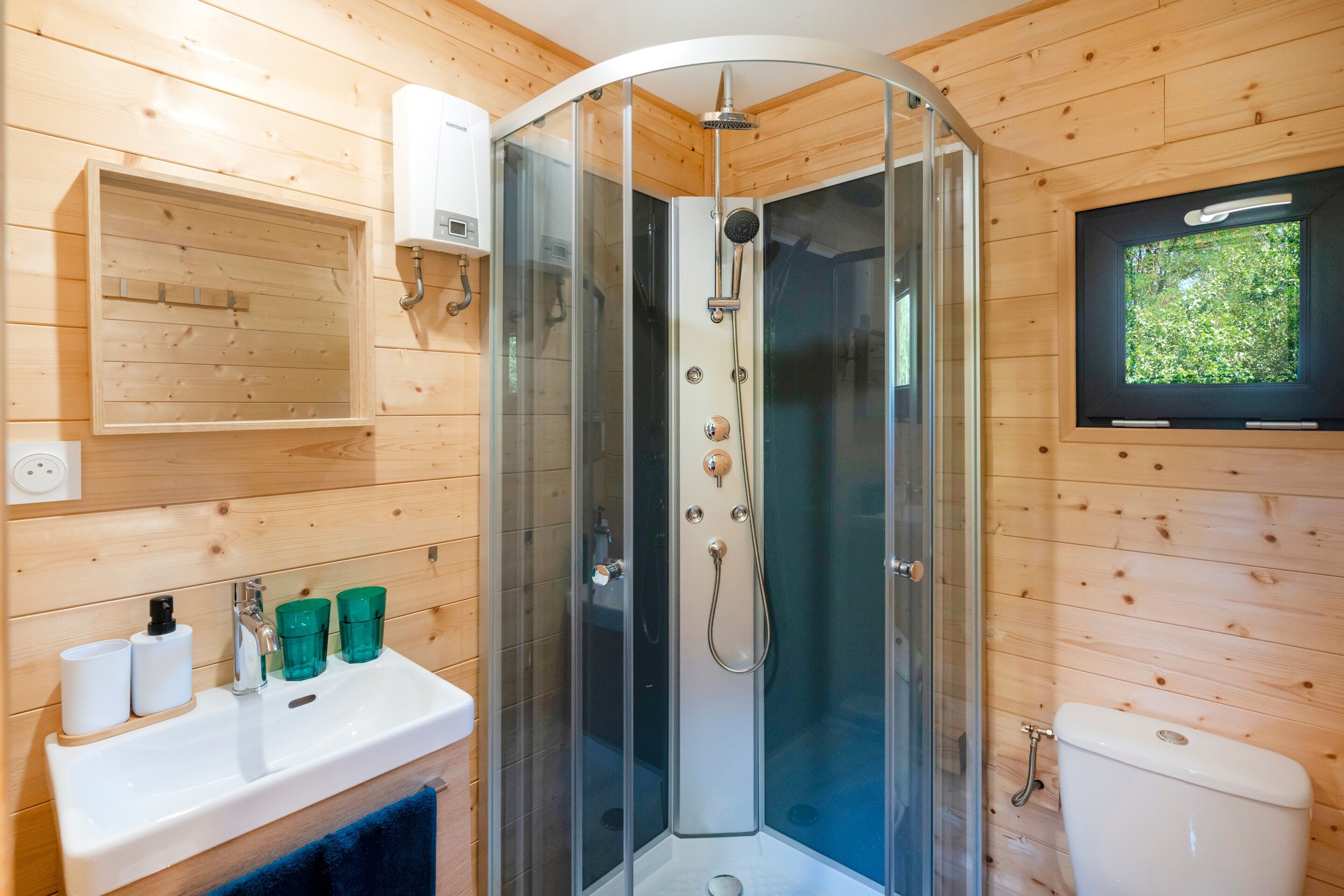 Een moderne badkamer met een douchecabine van glas, houten wanden, een wastafel met toiletartikelen en een toilet.