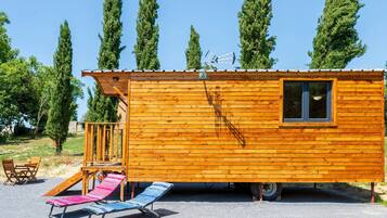 Een houten hut met een raam, een klein terras en een glijbaan.