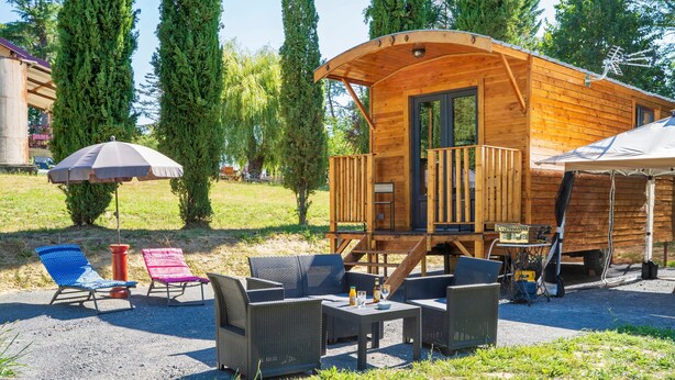 Eine Holzhütte mit Balkon, Sitzgelegenheiten im Freien und einer überdachten Terrasse mit Sonnenschirmen.
