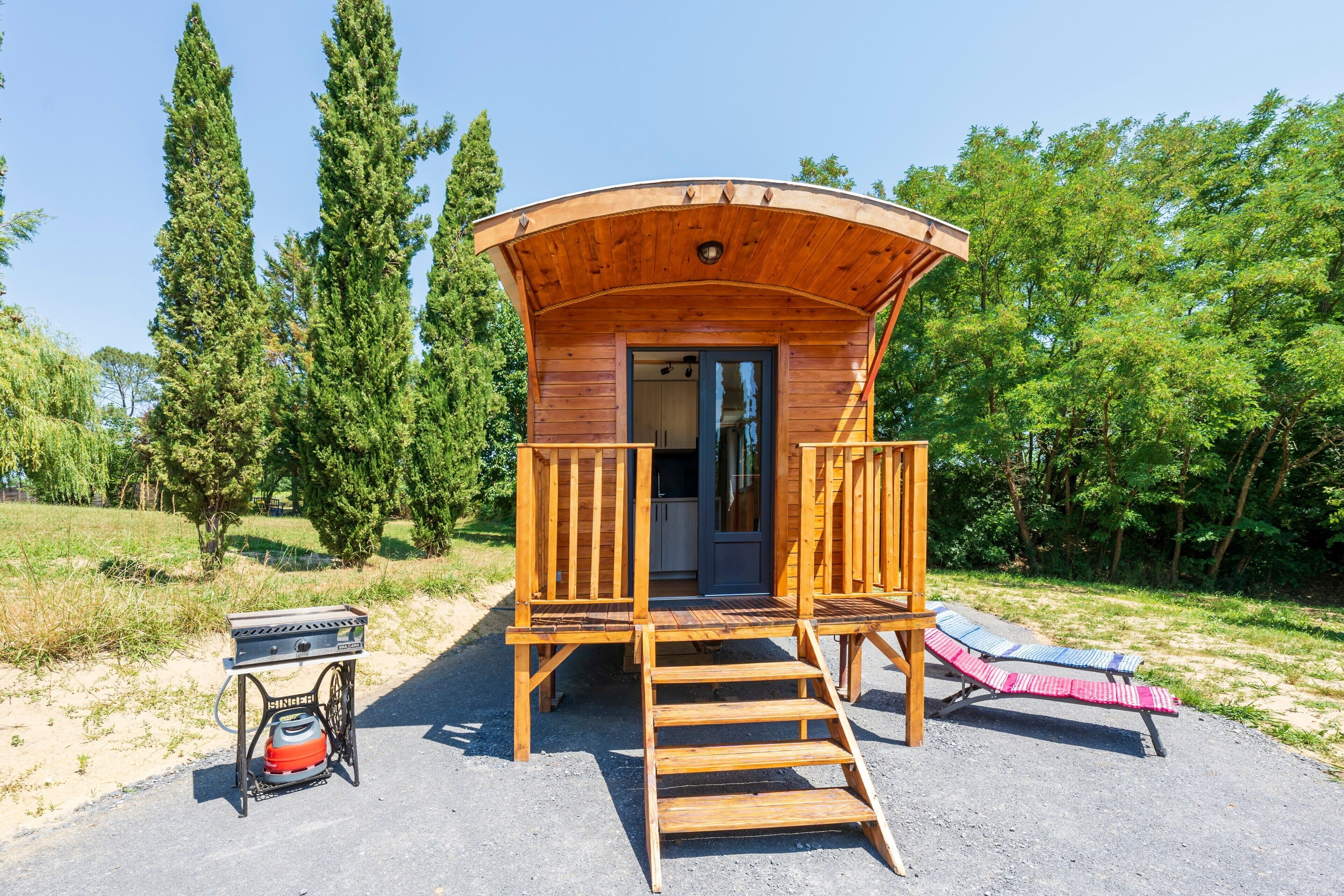 A wooden cabin with a curved roof, a staircase leading to a door, and a small outdoor seating area with a grill.