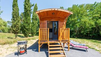 A wooden cabin with a curved roof, a staircase leading to a door, and a small outdoor seating area with a grill.