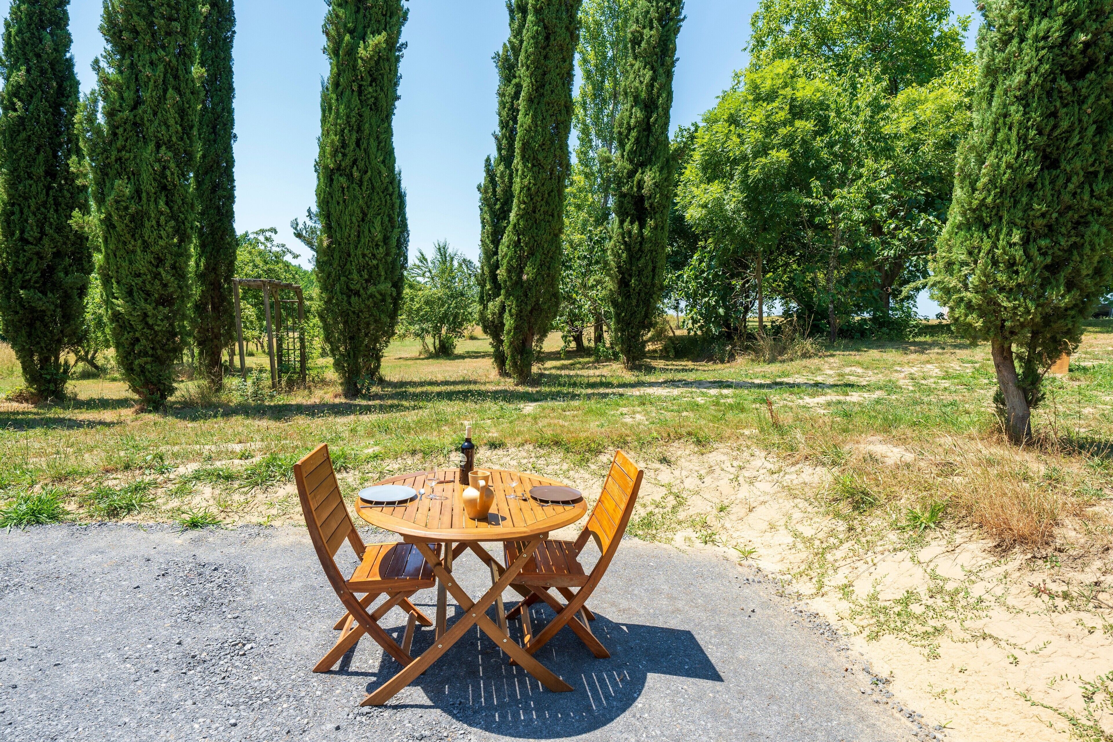 Een ronde houten tafel met stoelen in een buitengebied, omringd door hoge bomen.