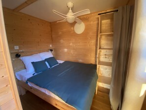 A wooden cabin room with a bed, a ceiling fan, and a window with curtains. - Tiny Home 'D'Artagnan De La Pausa Verda' with Shared Terrace, Private Garden and Wi-Fi (Montréal)