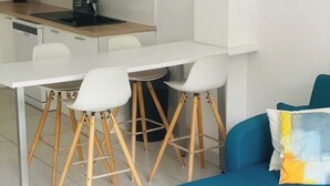 Une cuisine moderne avec des meubles blancs, une table à manger avec quatre chaises et un canapé bleu avec un coussin.
