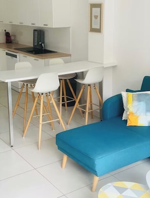 Une cuisine moderne avec des meubles blancs, une table à manger avec quatre chaises et un canapé bleu avec un coussin.