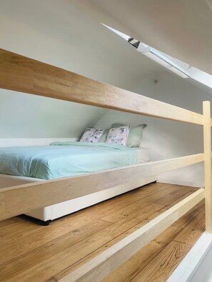 Camera da letto in stile loft con soffitto a falde, un letto con copripiumino azzurro e pavimento in legno.