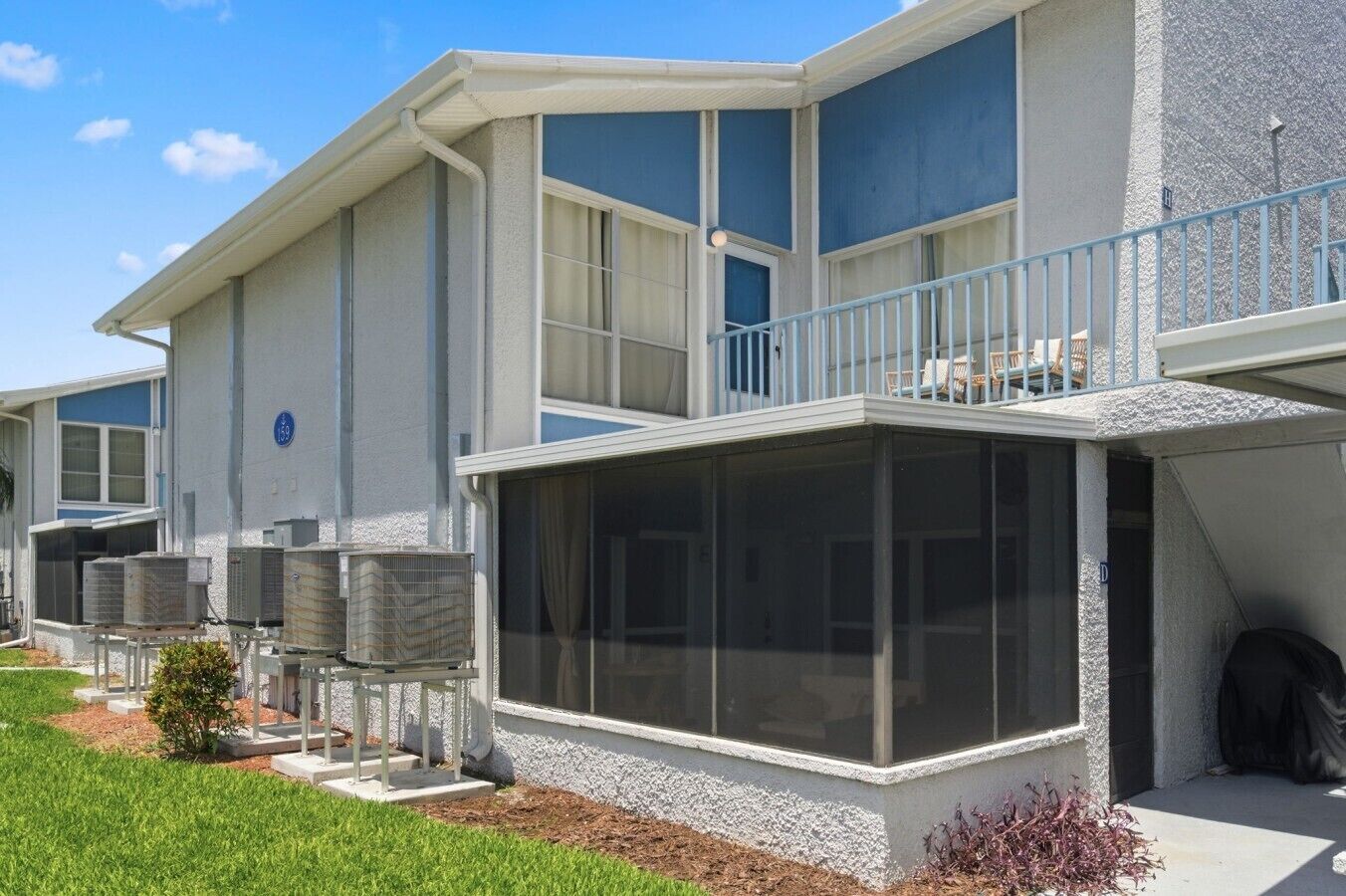 Un edificio residencial de varios pisos con balcón, ventanas grandes y unidades de aire acondicionado.