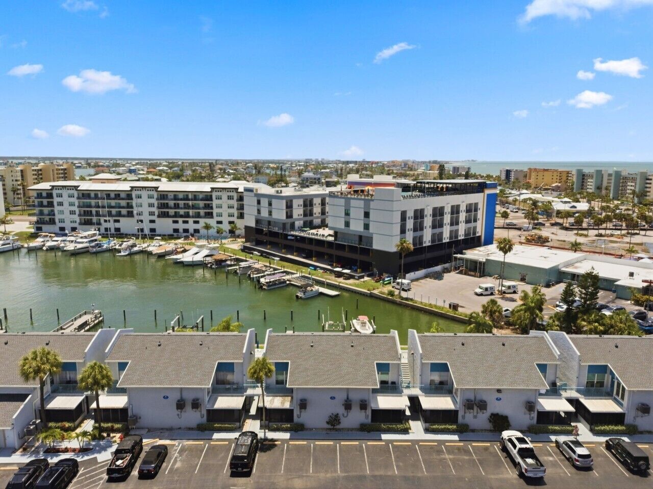 Un puerto deportivo con barcos amarrados, un edificio de varios pisos y un estacionamiento con automóviles.