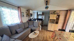 A modern living room with a grey sectional sofa, a small round coffee table, and a dining table with a poppy-patterned tablecloth. - Mobil-Home 417 6 persons (Litteau)