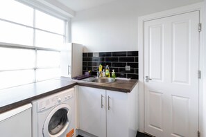A compact kitchen with a built-in washer, a sink, and a white door. - 3BR Flat in Hyde Park Area, Steps Away from Oxford Street (London)