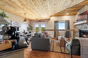 Ein gemütlicher Wohnbereich mit Kamin, einer Couch, einem Couchtisch und einer Küchenzeile mit Töpfen und einer Pflanze.
