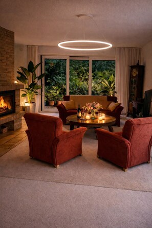A living room with a fireplace, a round table with candles, and a view of greenery outside. - Fantastic, stylish house with large garden on the North Sea coast. (Schortens)