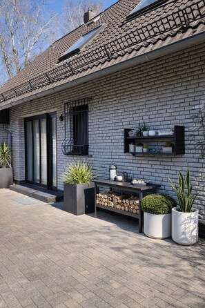 A modern house with a brick facade, a tiled roof, and a small outdoor seating area with plants and a lantern. - Fantastic, stylish house with large garden on the North Sea coast. (Schortens)