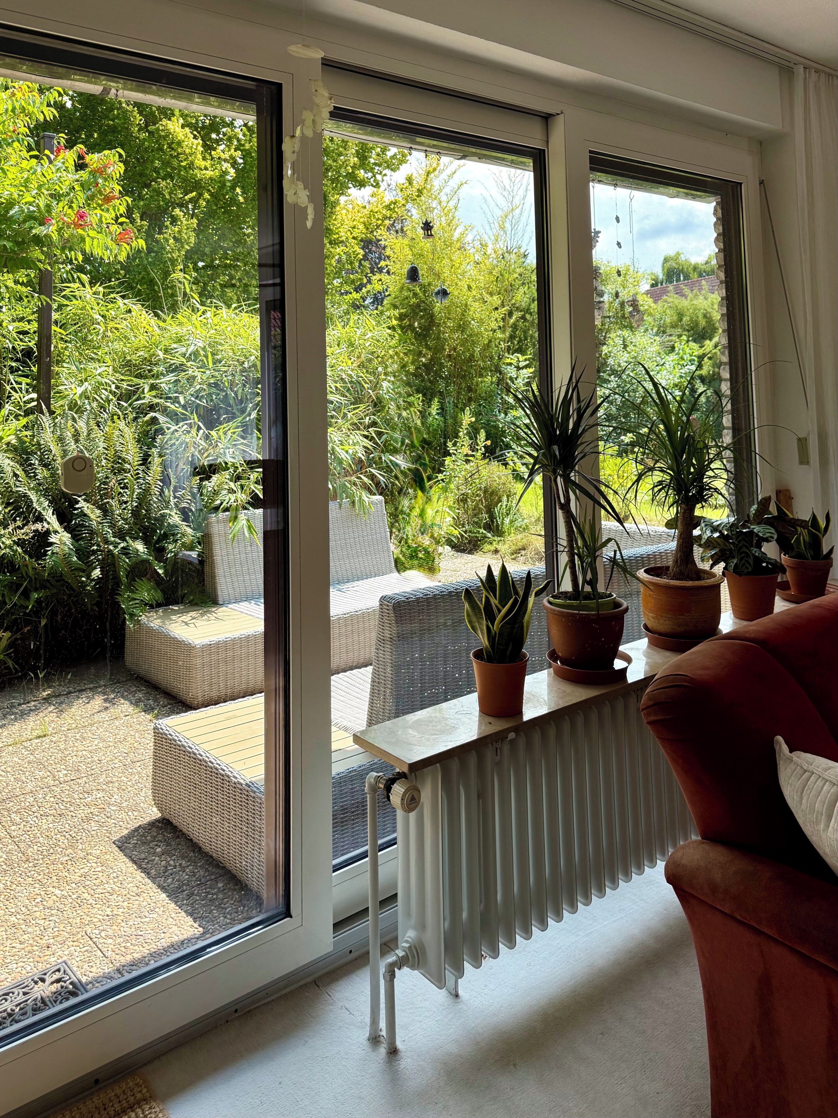 A room with a large sliding glass door leading to a garden, a radiator, and a brown sofa.