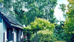 Ein traditionelles Gebäude mit einem geneigten Dach, umgeben von üppigem Grün und blühenden Pflanzen.