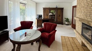 Ein Wohnzimmer mit Kamin, Fernseher, Esstisch und roten Polstersesseln.