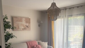 A living room with a sofa, a coffee table, a hanging light fixture, a wall-mounted lamp, and a large window with curtains. - T2 Puy de Dôme Chic, Cozy & Ideally Located (Clermont-Ferrand)