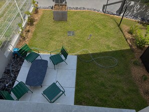 Une terrasse avec une table et des chaises, une petite pelouse et un parterre de fleurs.