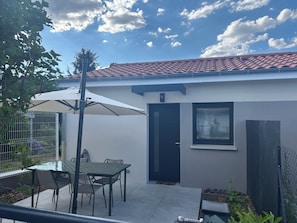 Eine Terrasse mit Tisch und Stühlen, eine überdachte Sitzgelegenheit, eine Tür und ein Fenster.