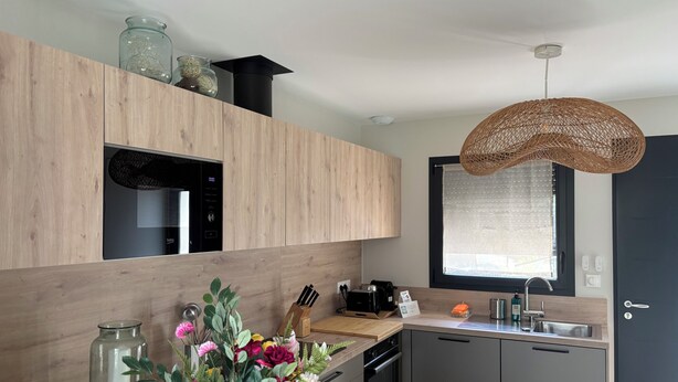 A modern kitchen with wooden cabinets, a built-in oven, a sink, and a hanging light fixture. - T2 Puy de Dôme Chic, Cozy & Ideally Located (Clermont-Ferrand)