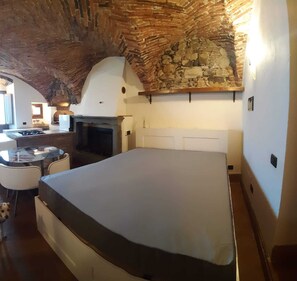 Ein Zimmer mit Steindecke, Kamin, Bett, kleinem Tisch und einem Hund.