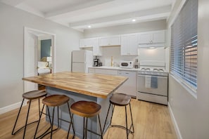 A modern kitchen with a wooden island, bar stools, white cabinets, and stainless steel appliances. - Downtown Haven|Patio|Near Dining (Vista)