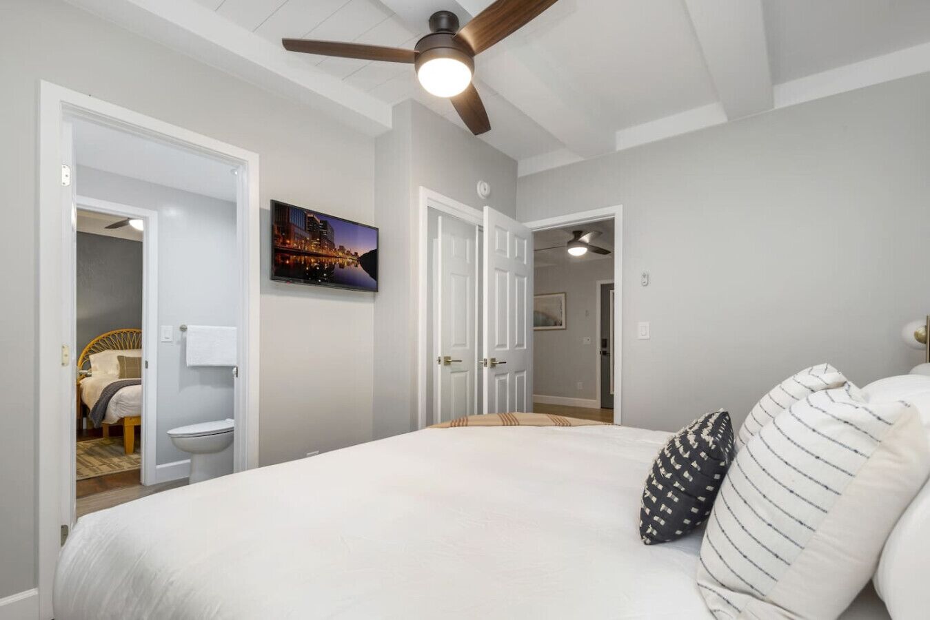 A bedroom with a large bed, a ceiling fan, and a cityscape painting on the wall.