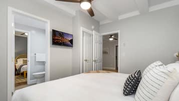 A bedroom with a large bed, a ceiling fan, and a cityscape painting on the wall.